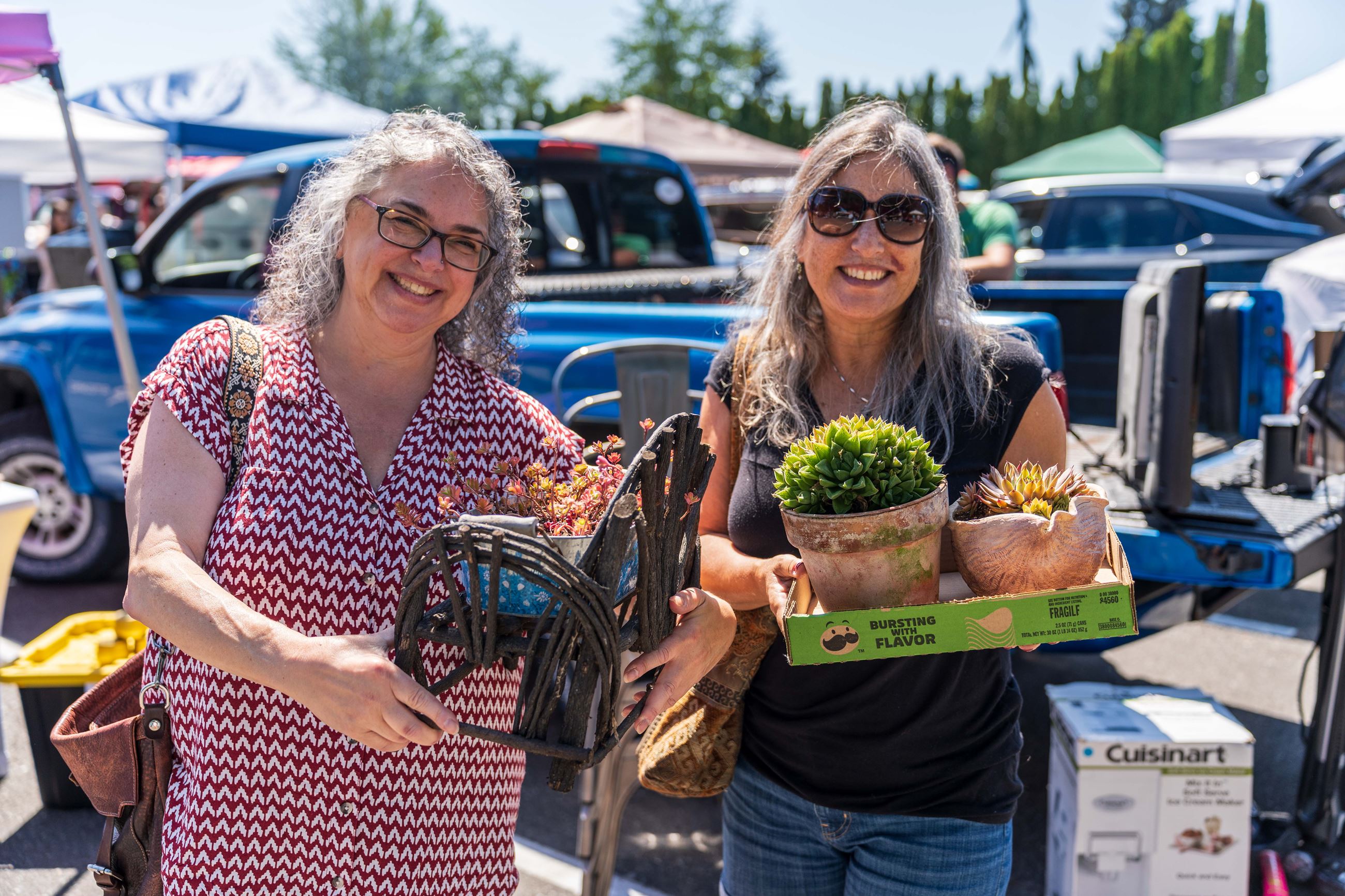 Two women at the junk in the trunk event holding plants and other purchased items from even