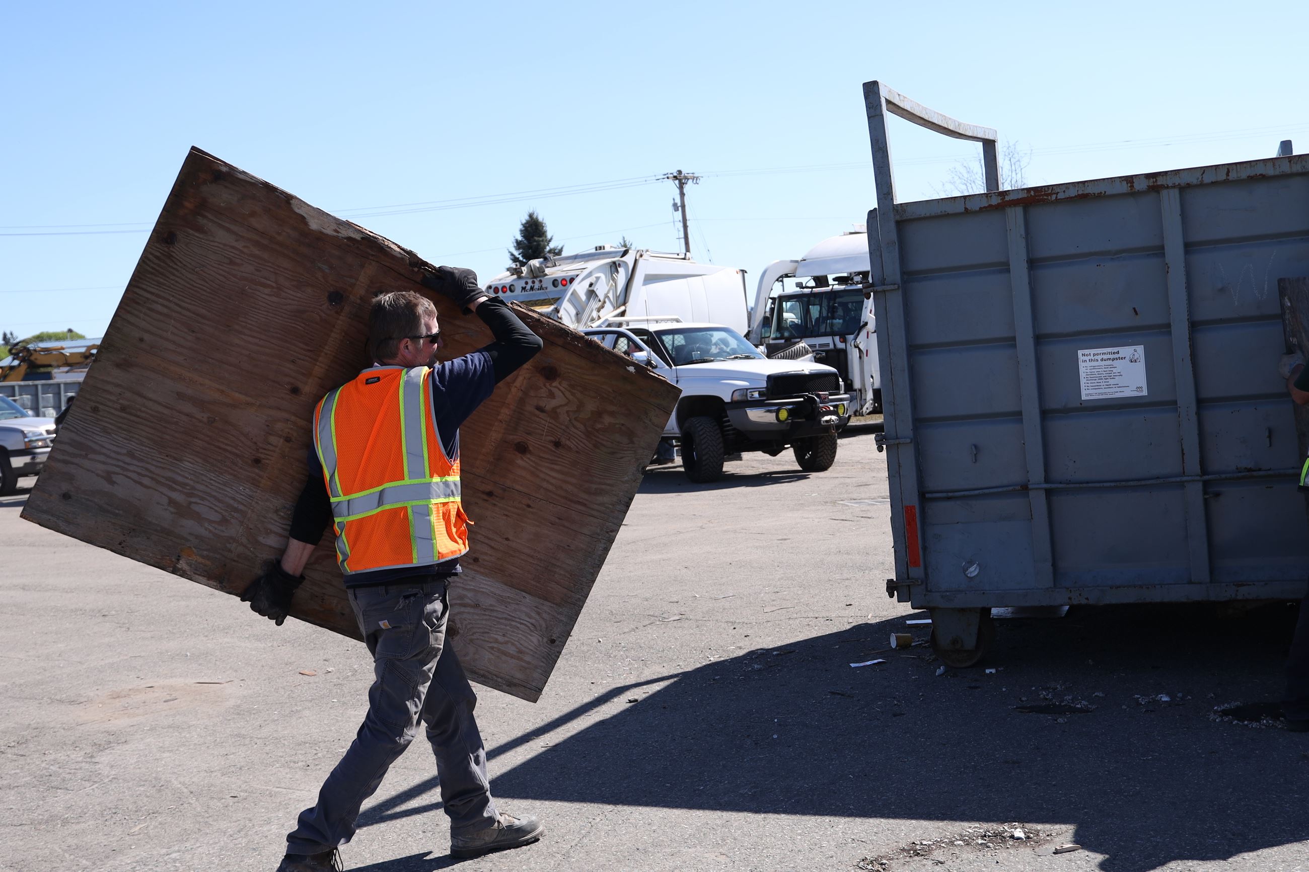 A city employee loading wood into a dumpster at an event